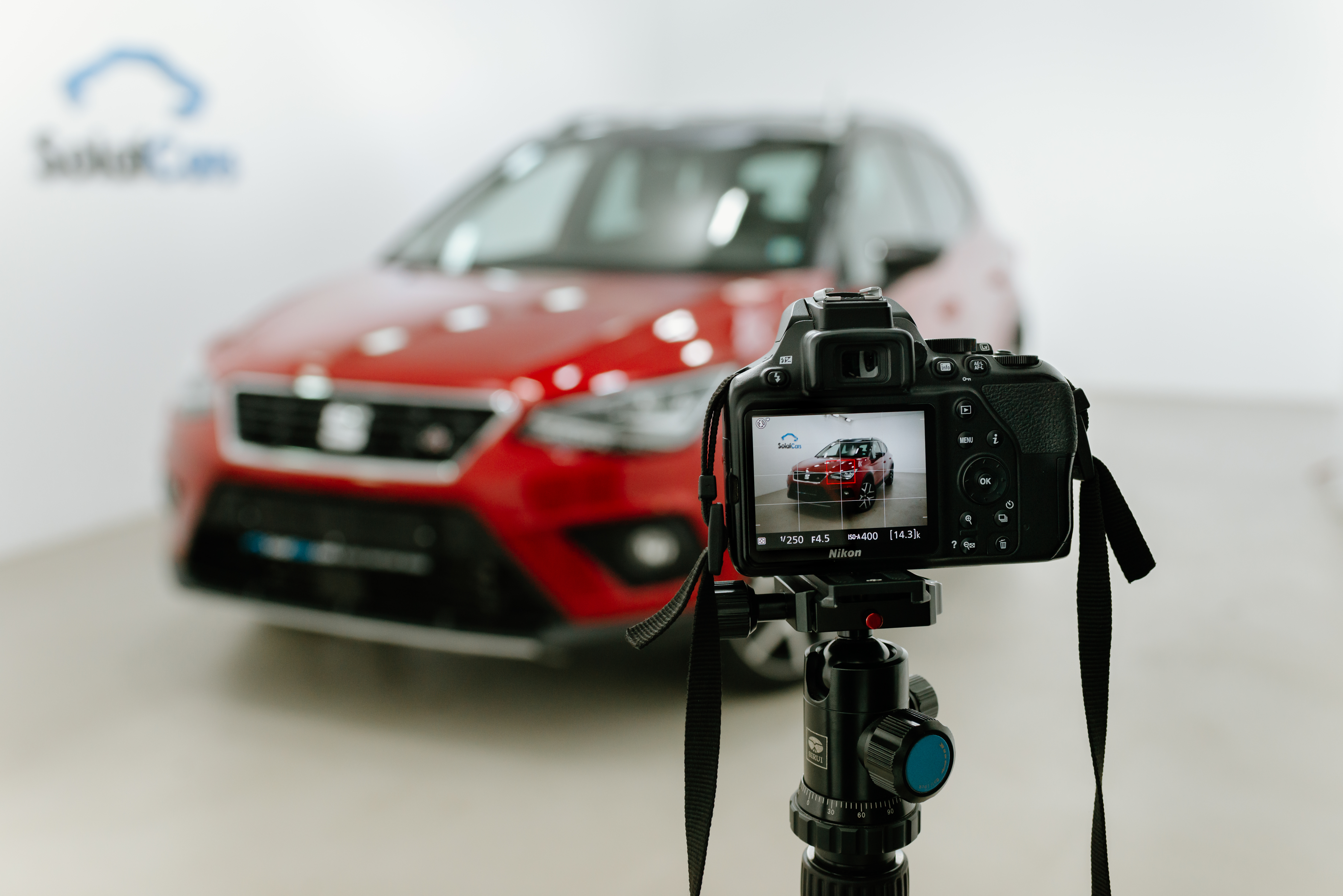 Dslr profi fényképezőgép állványra helyezve egy piros autó előtt