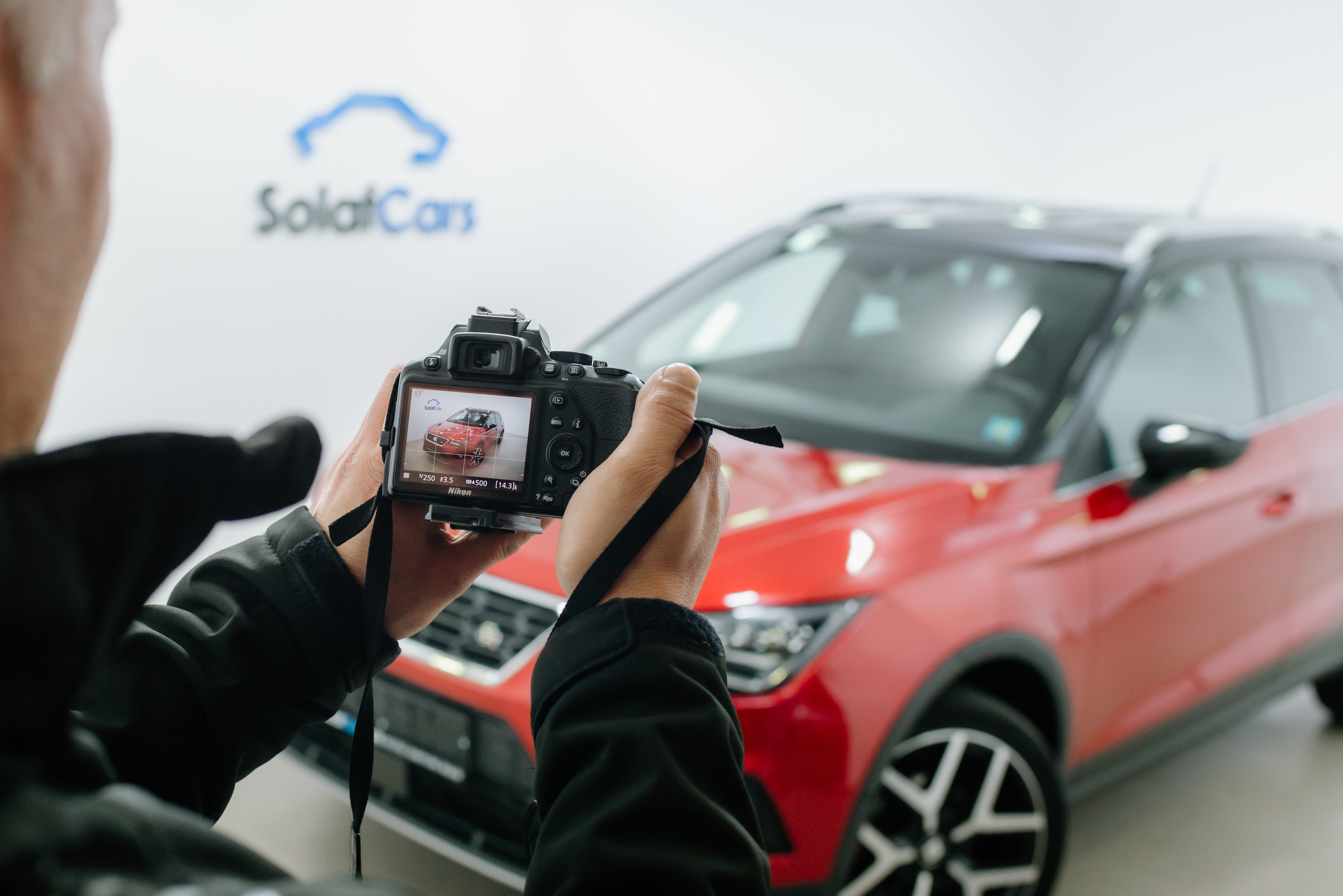 Közelkép egy férfiról, aki dslr kamerával fényképez egy piros autót egy fotóstúdióban